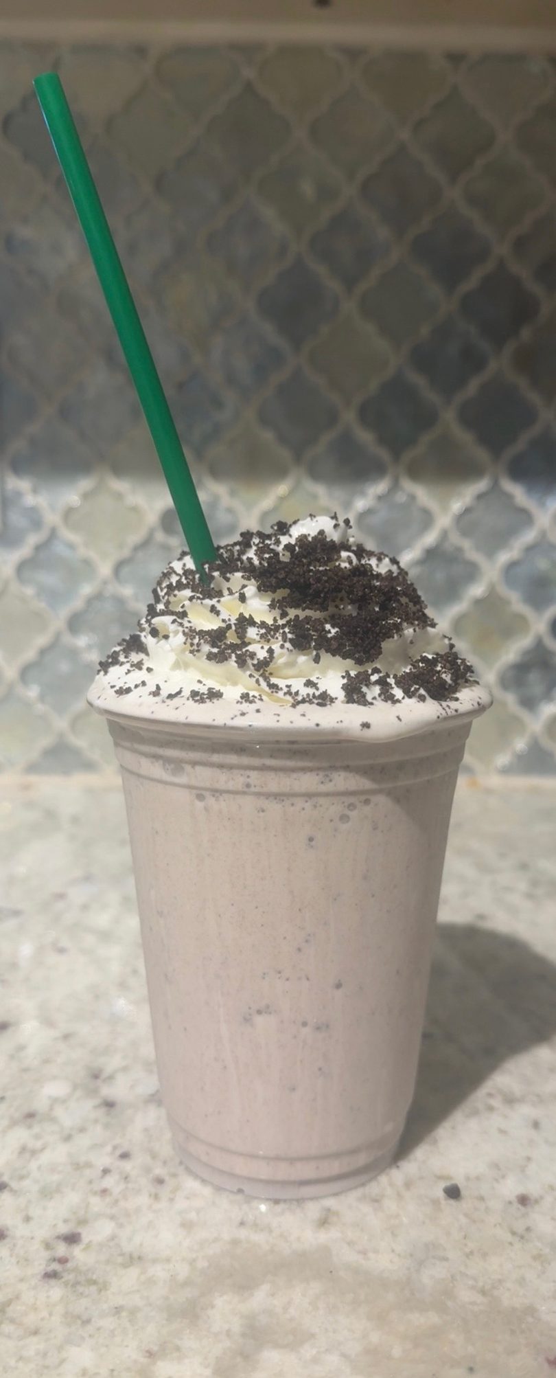 A cookies and cream milkshake with whipped cream, cookie crumbles, and a green straw.