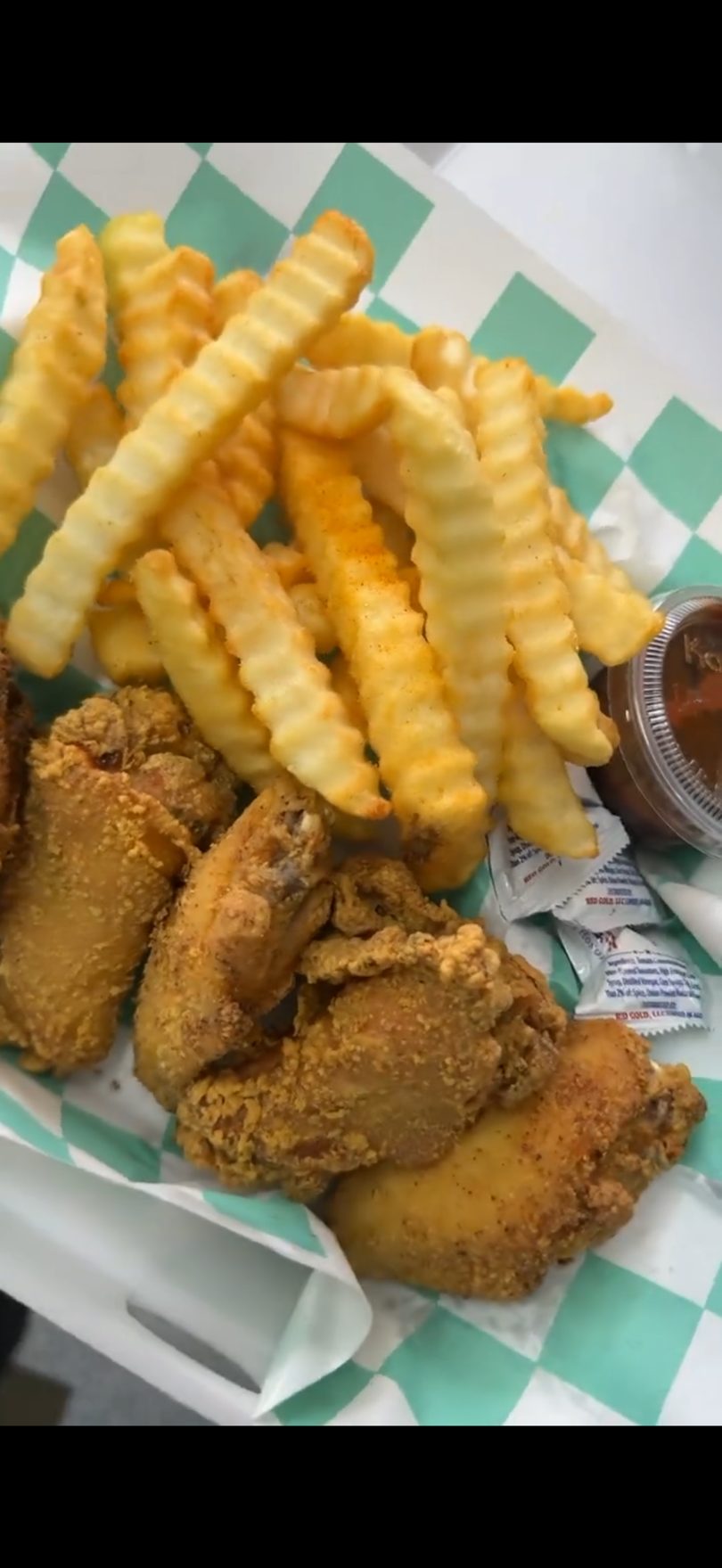 Crispy fried chicken wings and crinkle-cut fries served in a checkered paper basket with sauce.