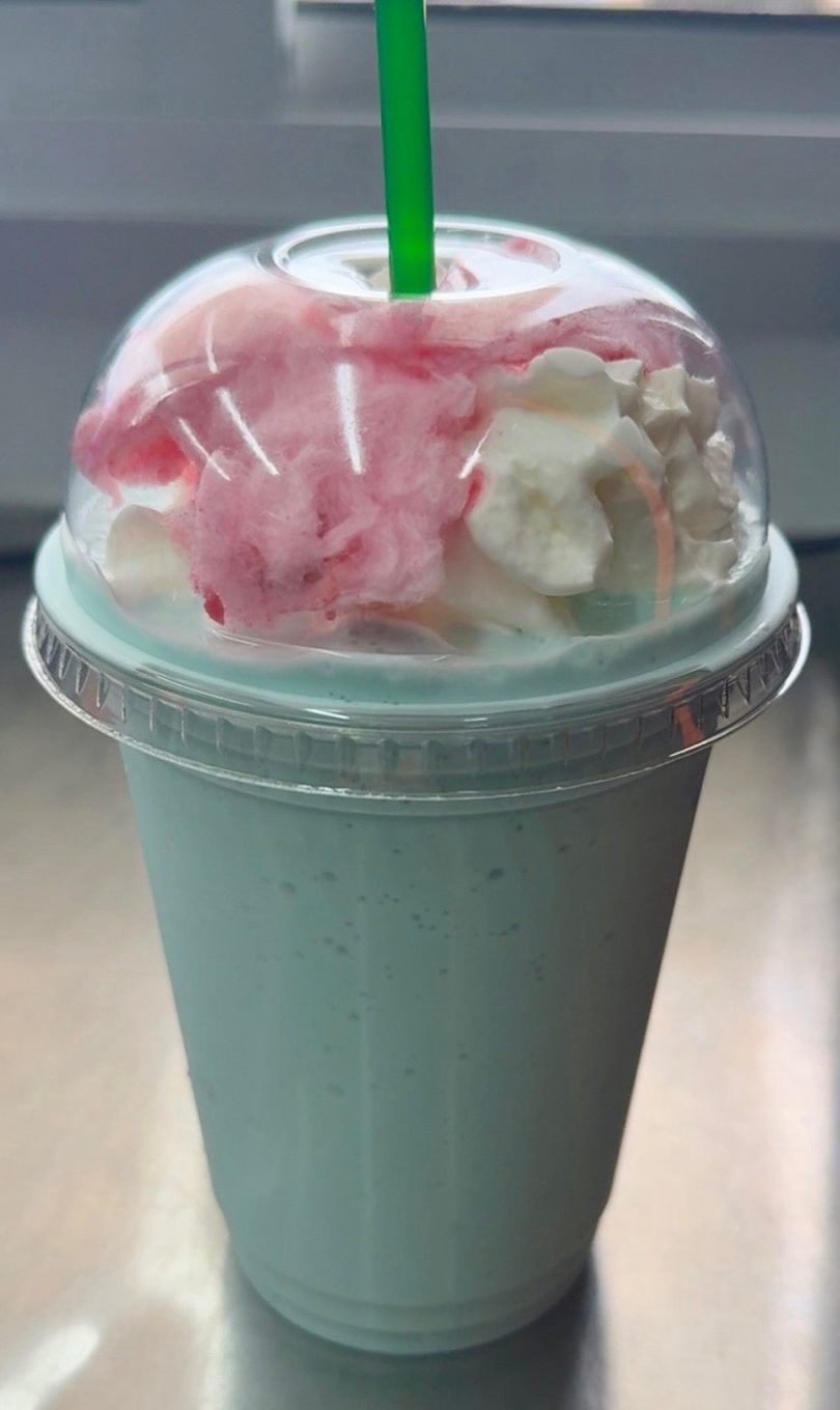 Light blue milkshake with whipped cream, pink cotton candy, and a green straw.