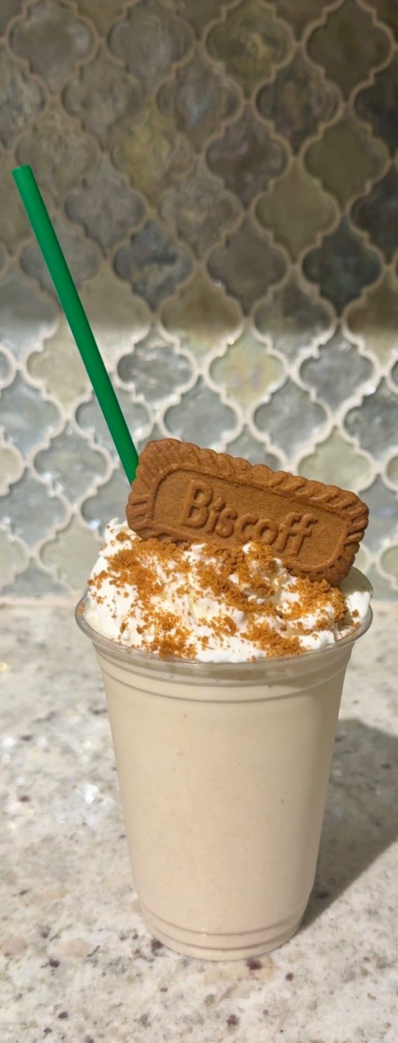 Biscoff milkshake topped with whipped cream, cookie crumbs, and a Biscoff cookie, with a green straw.