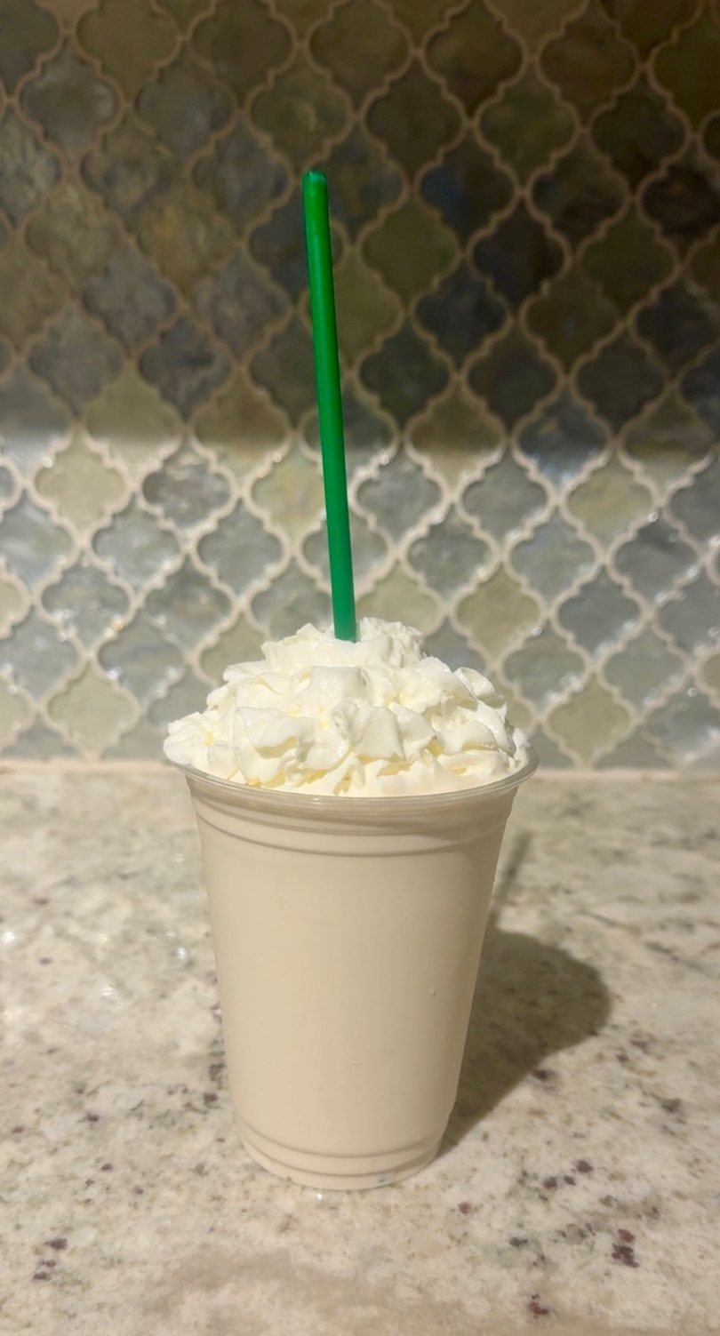 A white cup filled with whipped cream and a green straw on a speckled countertop.